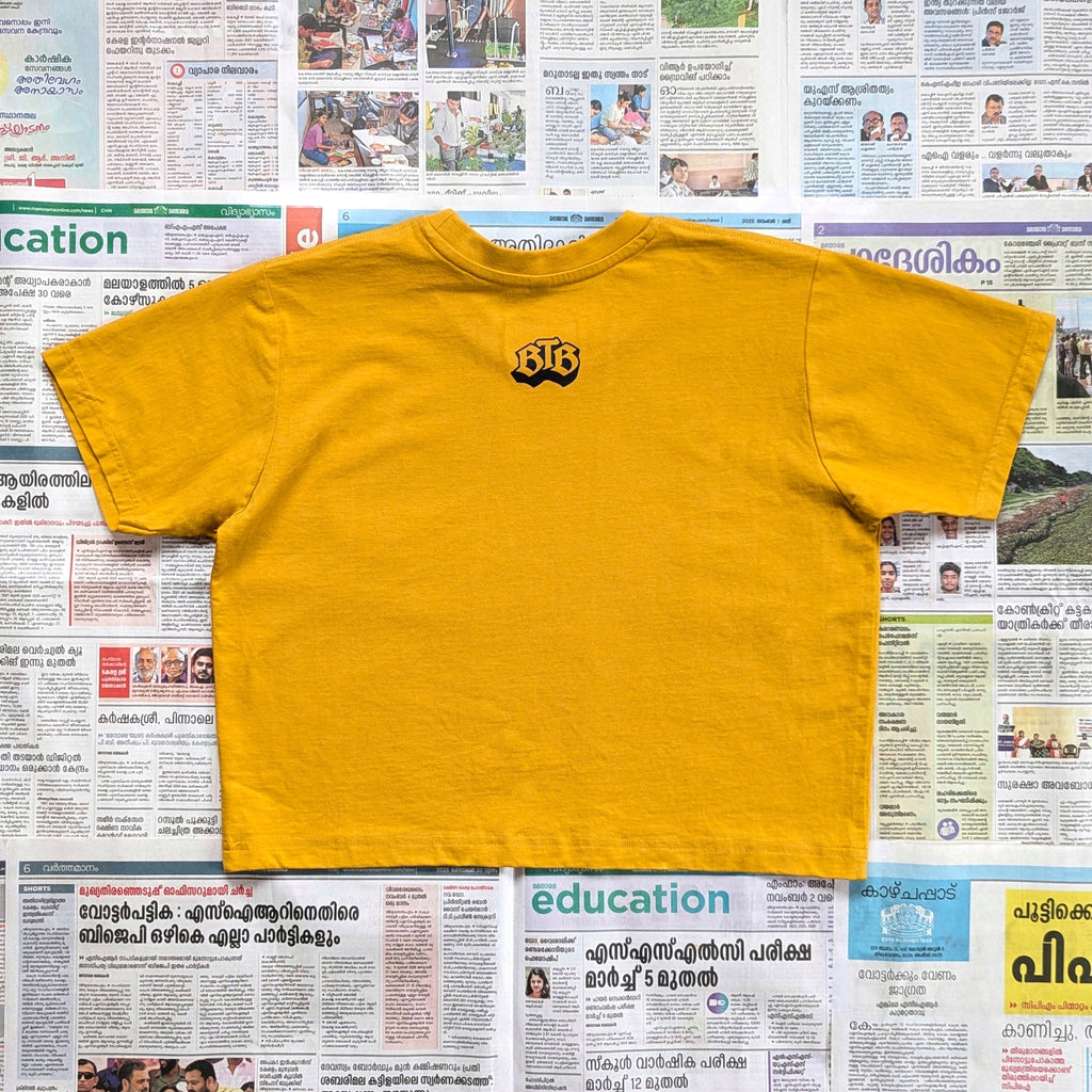 Mustard yellow crop top with a 'BTB' monogram on the back neck area